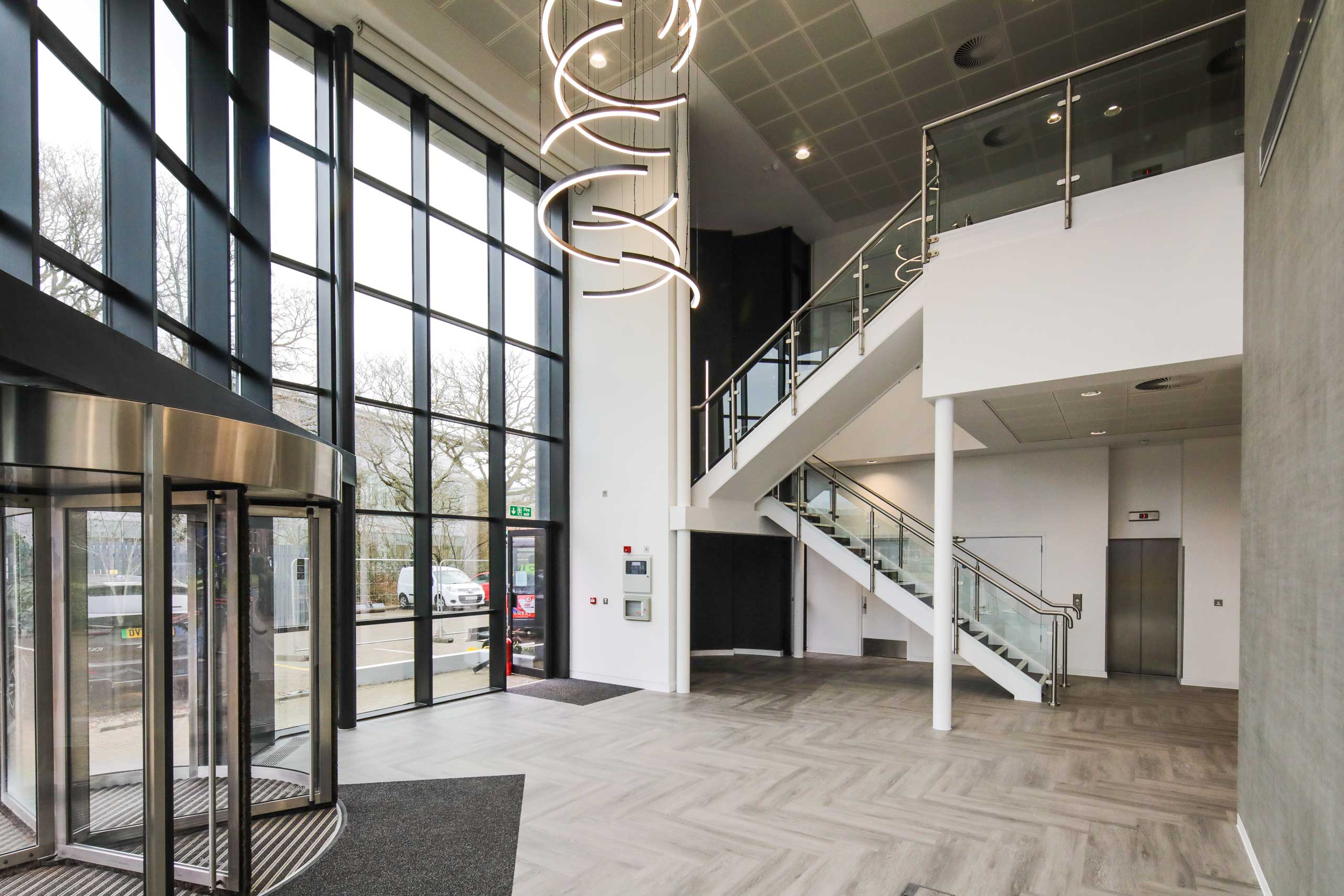 Modern office lobby with glass entrance, spiral staircase, and elevator on the right side.