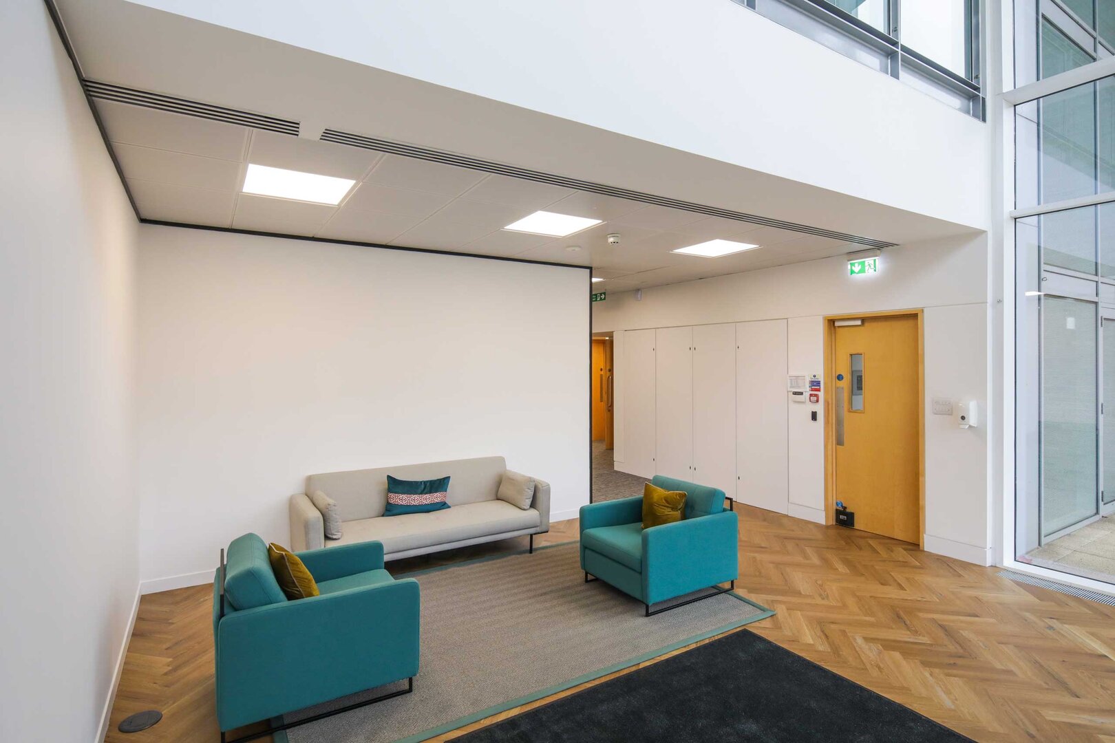 Modern office waiting area with a sofa, two armchairs, and a rug on a wood-patterned floor.