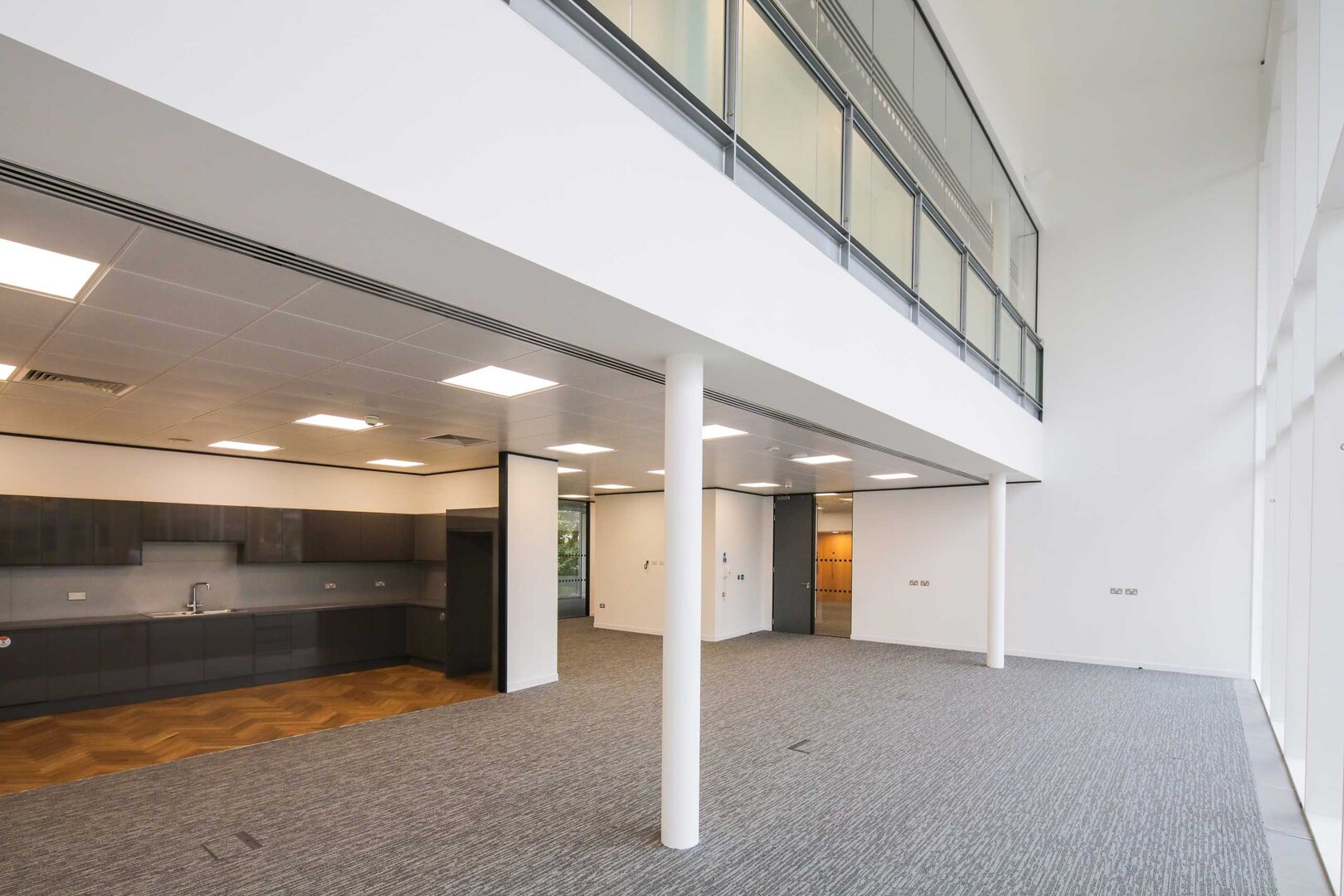 Modern empty office space with kitchenette, large windows, and a mezzanine level.