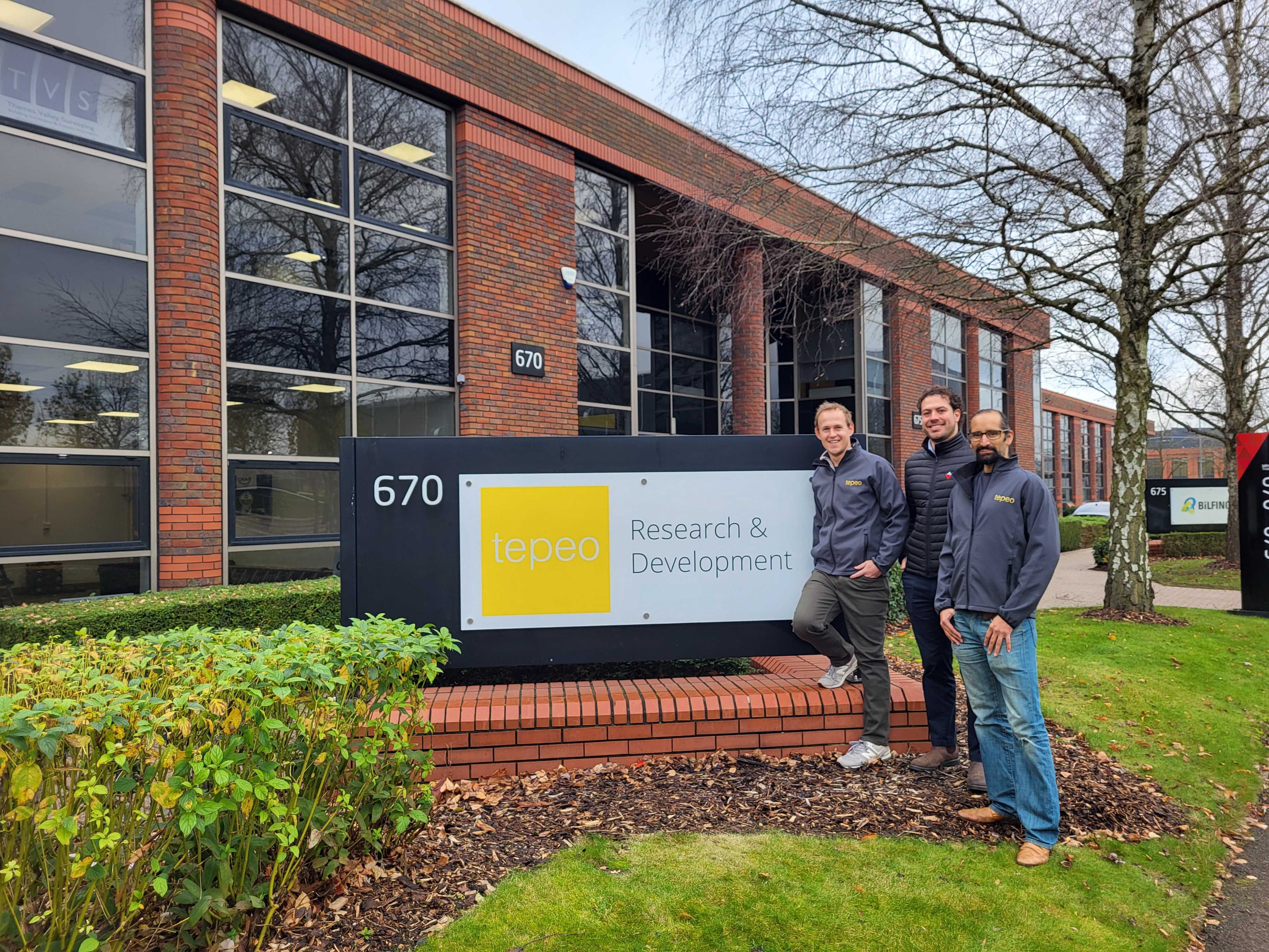 Three men standing in front of a building with a sign.
