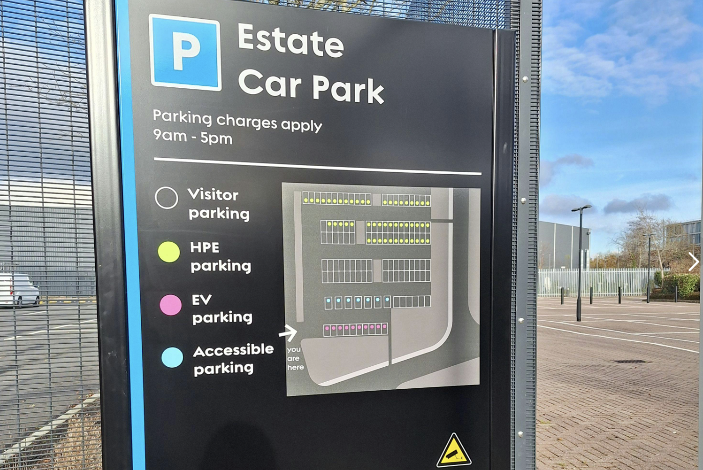 Parking sign with a map indicating visitor, HPE, EV, and accessible parking areas. Parking charges apply from 9am to 5pm.