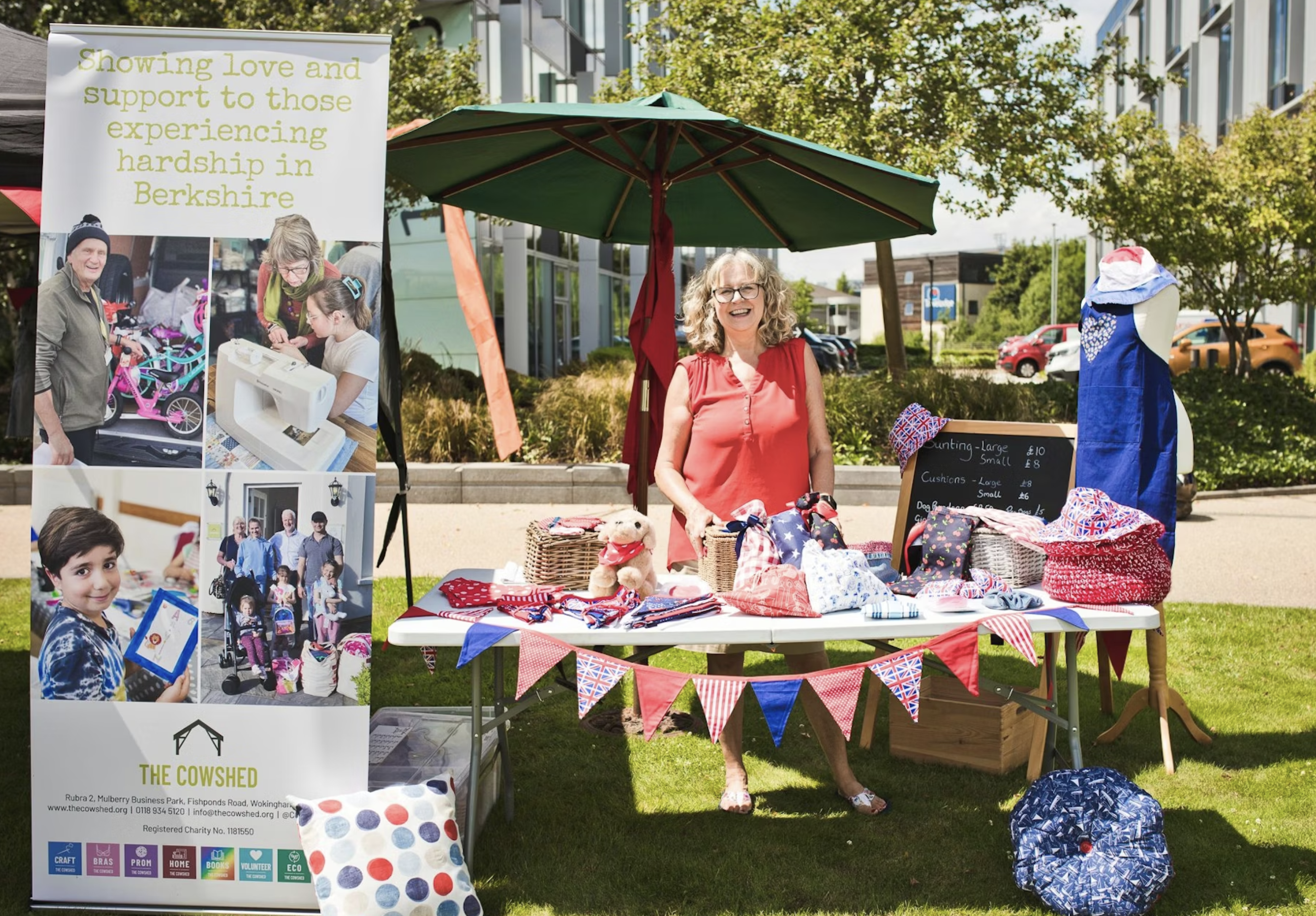 A woman stands behind a craft stall with handmade goods at an outdoor fundraising event.