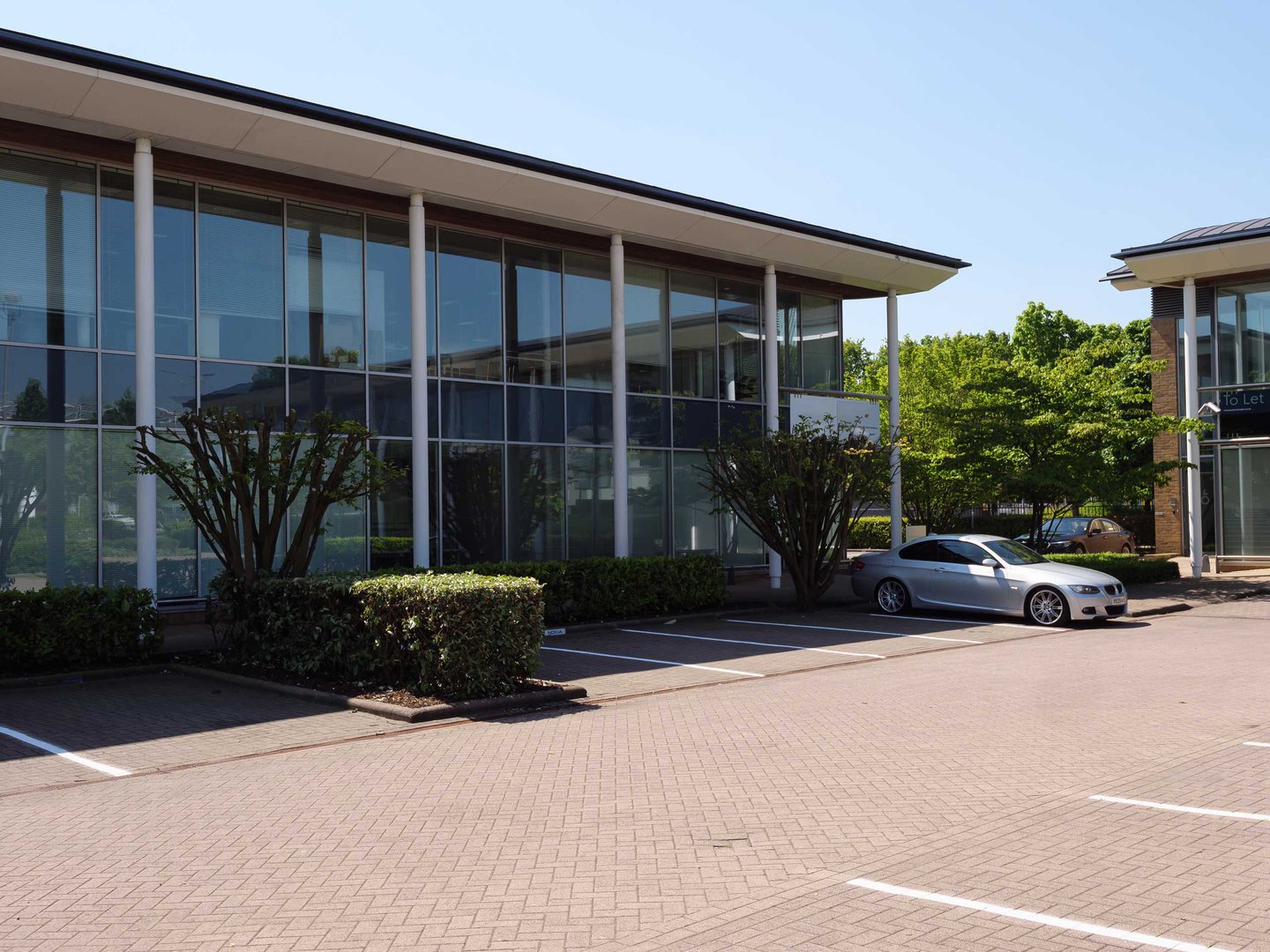 Silver car parked in front of a modern glass office building on a sunny day.