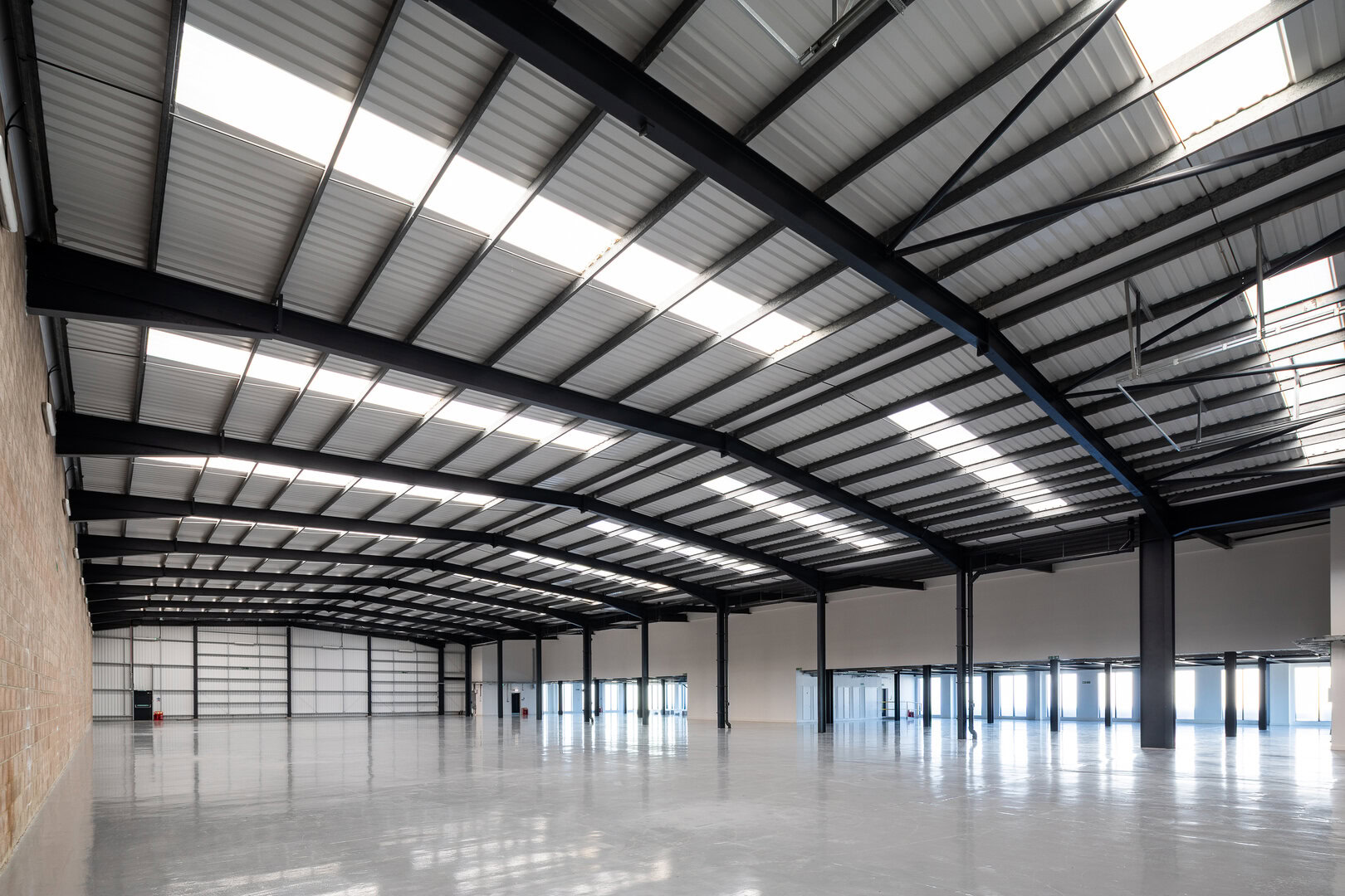 Large, empty warehouse with high metal ceiling, exposed beams, and polished concrete floor.