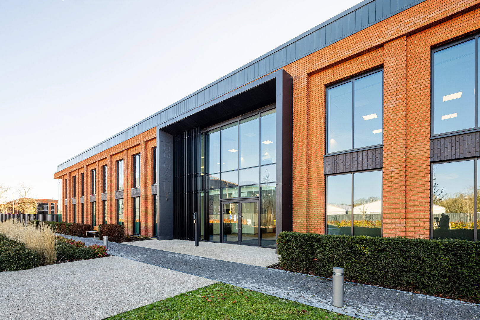 Modern brick office building with large glass entrance and neatly landscaped surroundings.