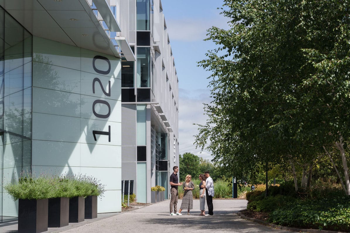 Four people stand talking outside a modern glass office building with the number 10200 displayed.