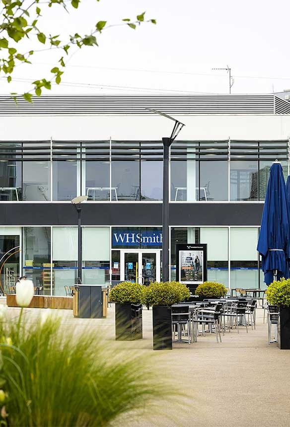 Outdoor seating area with tables and chairs in front of a modern building that has a WHSmith shop on the ground floor.